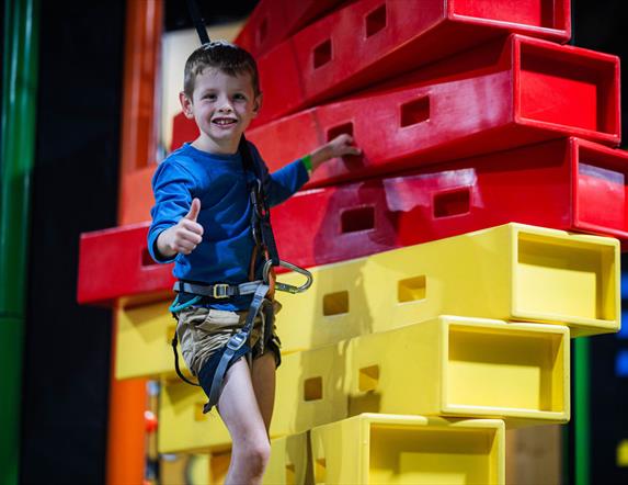 Boy in harness climbing up stacked blocks