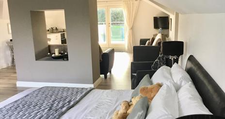 Image shows double bed with teddy bears and sitting area with patio doors to outside