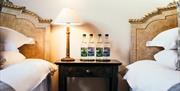 Image shows twin bedroom with beside table, lamp and 4 water bottles