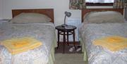 Image shows twin bedroom with beside table and lamp between beds