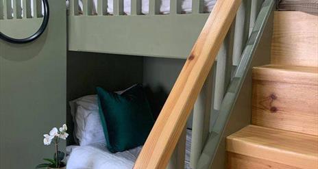 Image is of loft bedroom with bunk beds with wooden stairs up to top bunk