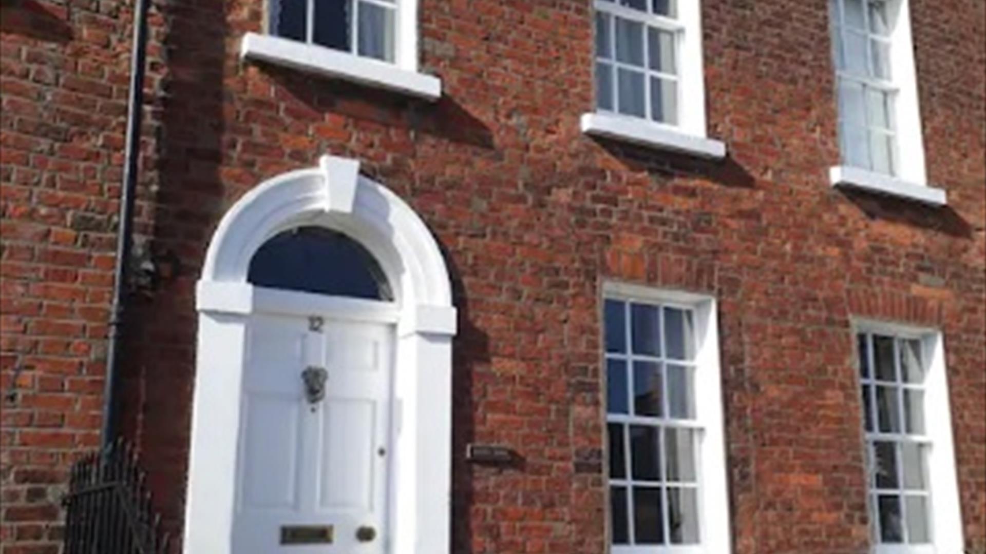 Image shows outside of property which is built in Georgian style with a white front door and sash windows. There are 2 small steps up to front door.