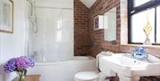 Image shows bath with overhead shower, brick feature wall, sink and toilet