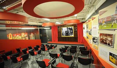 Image is of a meeting room with lots of chairs, images on the walls and large film screen on a stage