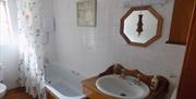 Image shows bathroom with low bath, overhead shower with curtain, toilet and sink with mirror above.
