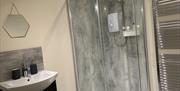 Image shows shower enclosure, tall radiator and sink in bathroom