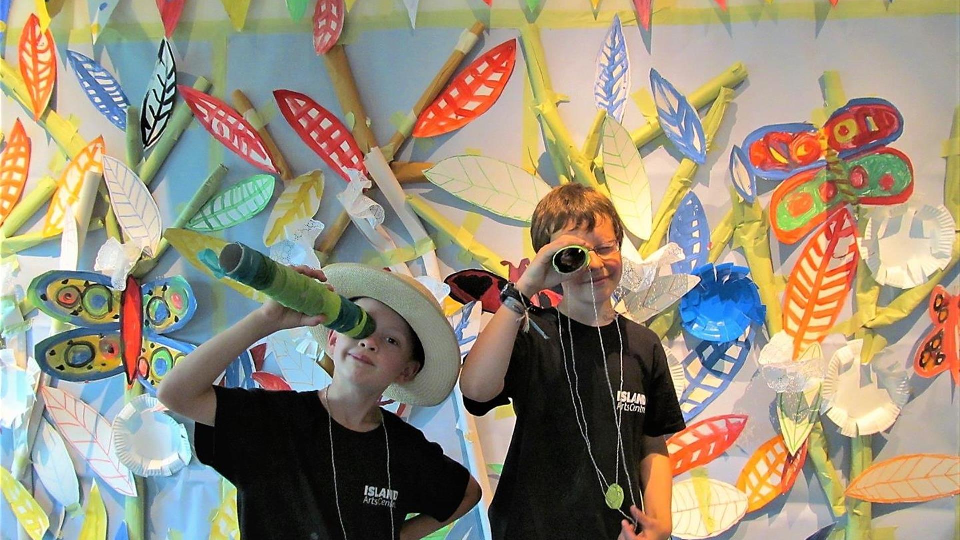 Two children playing with binoculars with art on the wall in the background