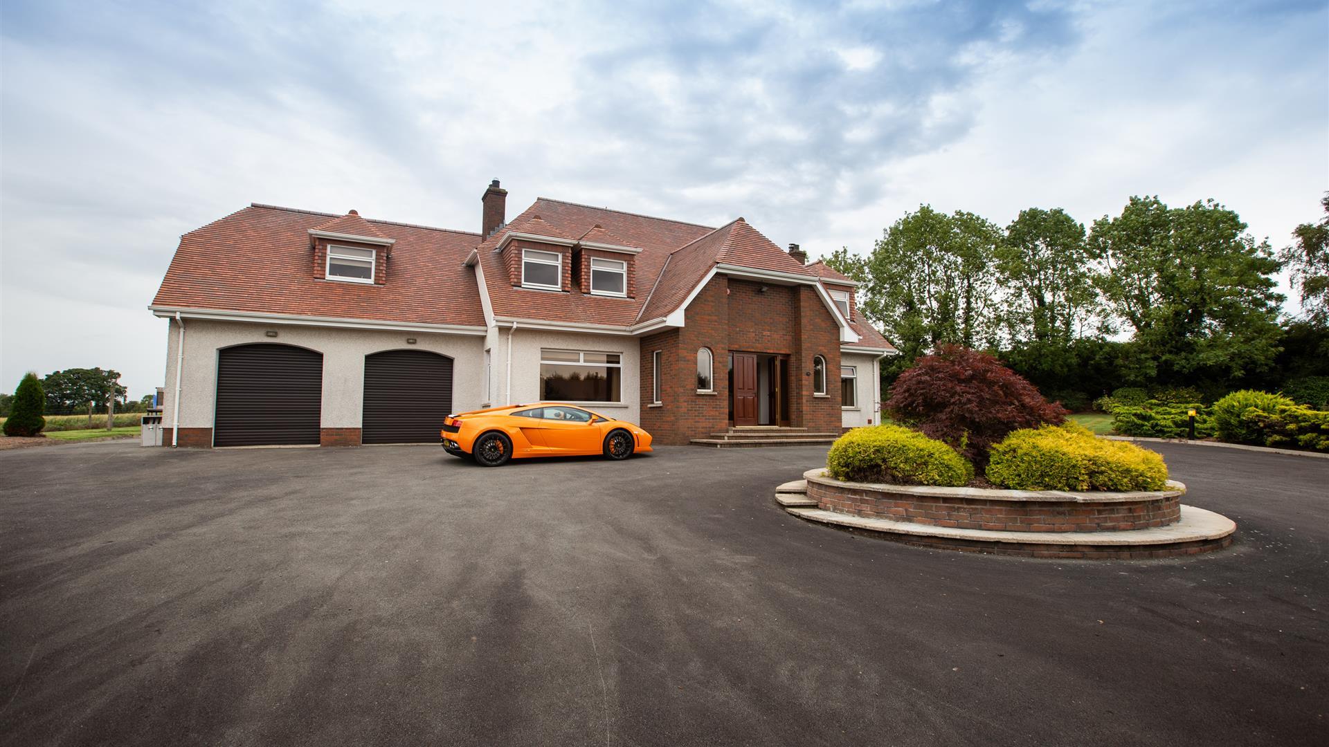 Image shows front of property with orange coloured super car in the large driveway