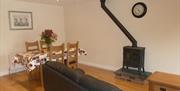 Image shows lounge area with sofa, wood burner, dining table and 4 chairs.