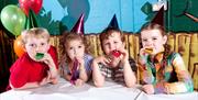 Image is of children sitting at a table with party hats on