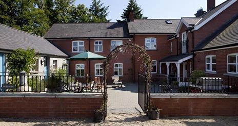 Image shows front of property with archway entrance and small courtyard with seating area