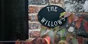Image shows signage for The Willows on a round slate on brick wall outside property