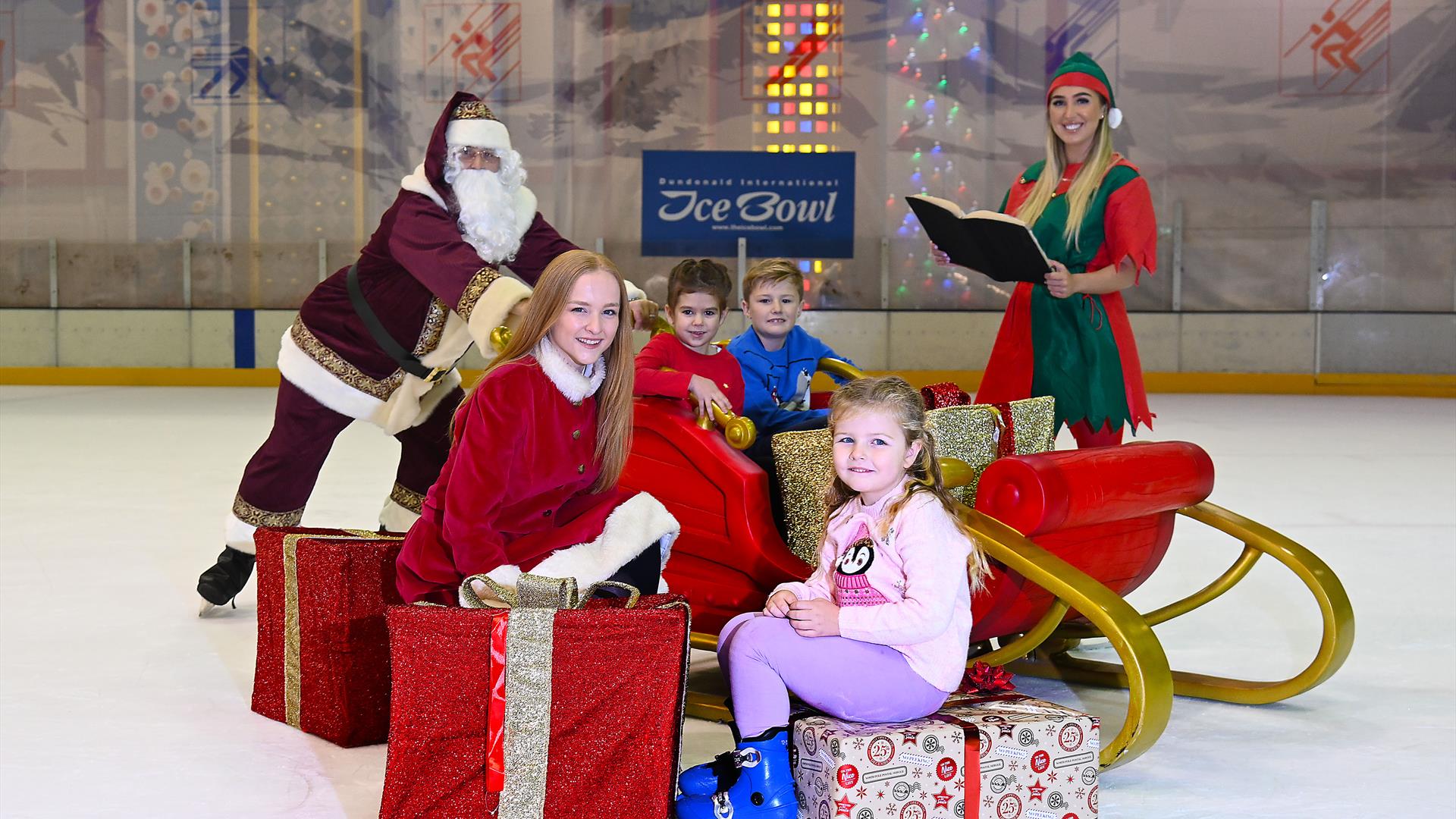 Santa pushing sleigh with two children on board, elf with book and two children sitting on Christmas Present.