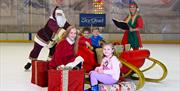 Santa pushing sleigh with two children on board, elf with book and two children sitting on Christmas Present.