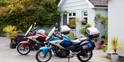 Image shows 2 motorcycles parked outside a cottage