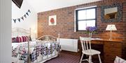 Image shows double bedroom with brick feature wall, white radiator, dressing table and chair