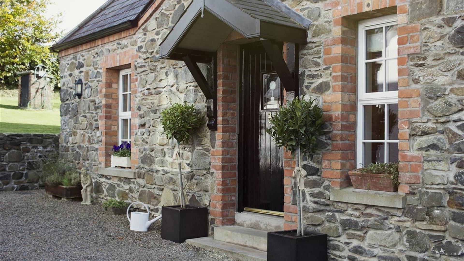Image shows outside of stone property with bay tree plants at either side of front door