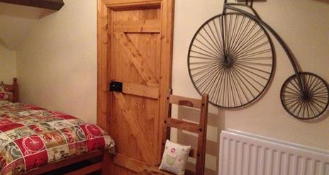 Image shows bedroom with pine door and replica penny farthing bicycle on the wall