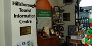 Image shows inside of visitor information centre with retail items on display and welcome to Northern Ireland map on the wall