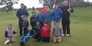Image shows group of adults and children posing for photo on the golf course