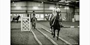 Black and white image of horses and riders inside a training course