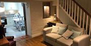 Image shows lounge area with sofa under the stairs, wooden floor and door way into kitchen open