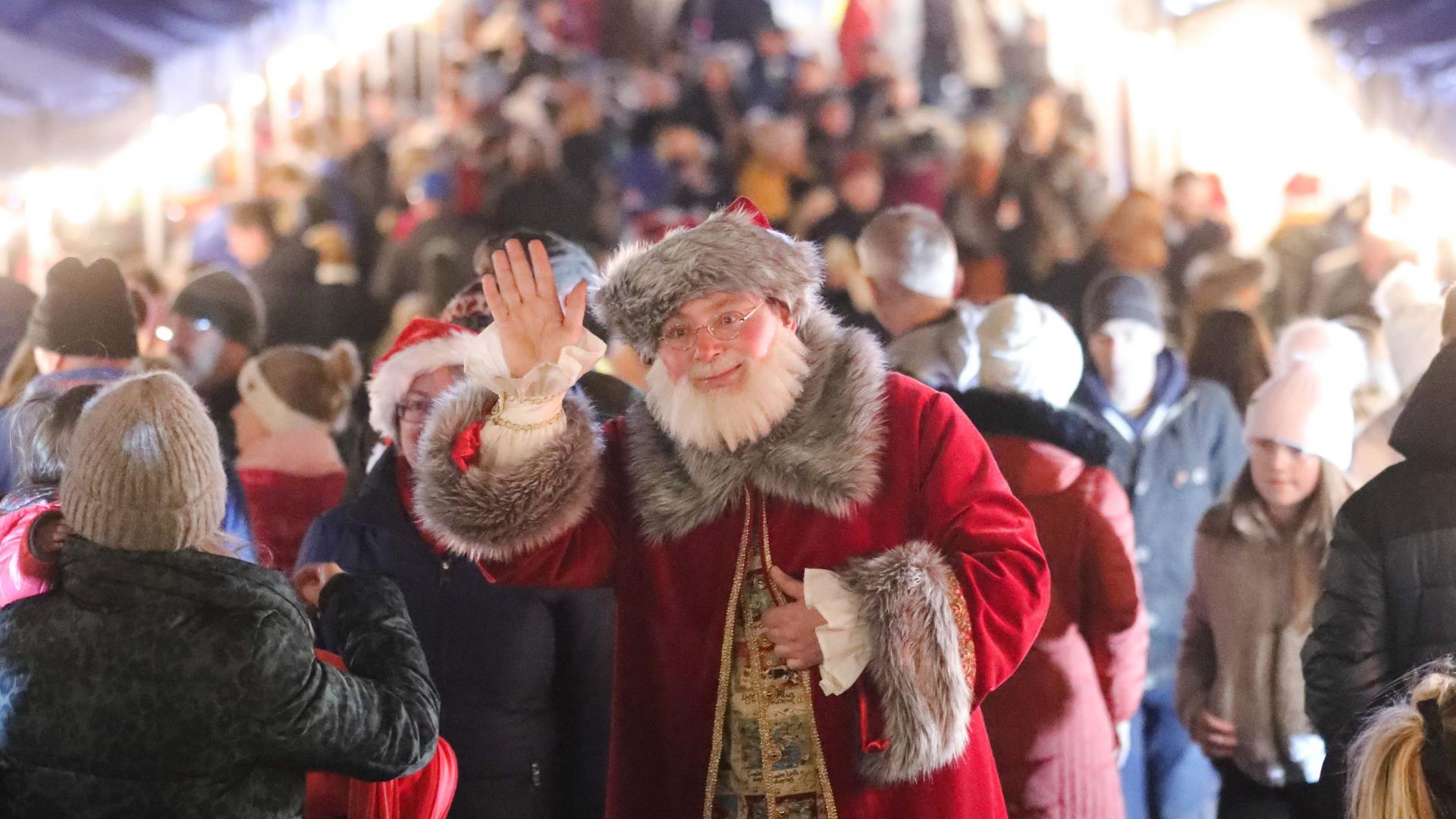 Santa waving at camera with crowd behind him