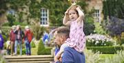 Child with a bee headband sitting on her father's shoulders in front of Hillsborough Castle