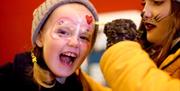 Image shows a young girl getting her face painted by an artist