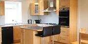 Image shows kitchen with a small island and 2 stools. All mod cons and dining table and chairs