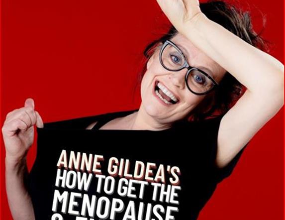 Picture of Anne Gildea holding a microphone above her head with a black top with the saying Anne Gildea's How to get the menopause & enjoy it