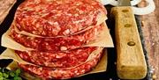 Image shows 4 raw beef burgers on a slab with a large knife beside them
