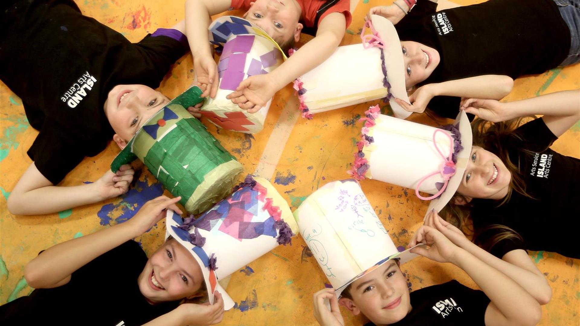 Children lying on floor wearing large hats