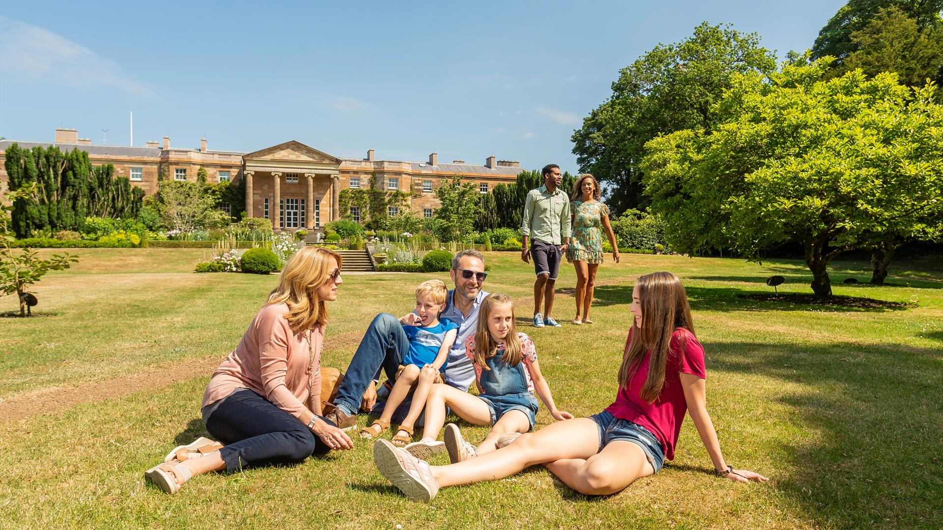 Family sitting on grass with Hillsborough Castle in background