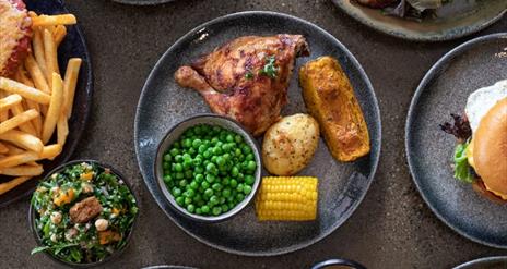 Image shows a few different dishes of food on plates - chicken, peas, burger and chips