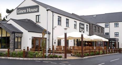 Image shows the exterior white building of Premier Inn Table Table Restaurant with a sign showing Linen House in grey and white writing and outside wo