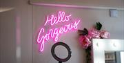 Image is of the interior of Linhol Beauty with a pink neon sign saying Hello Gorgeous
