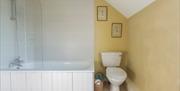Image shows bath with overhead shower attachment and toilet