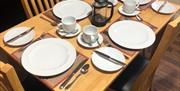 Image shows dining table and 4 chairs. Table is laid out for a meal
