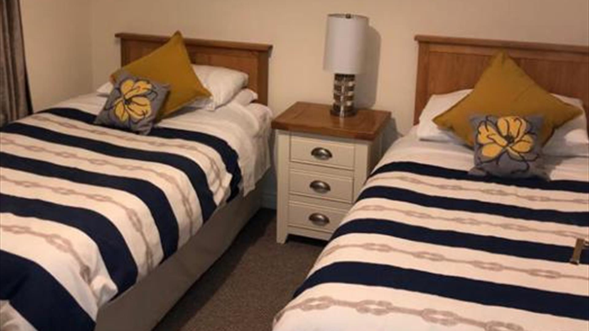 Image shows twin bedroom with bedside table and lamp between the beds
