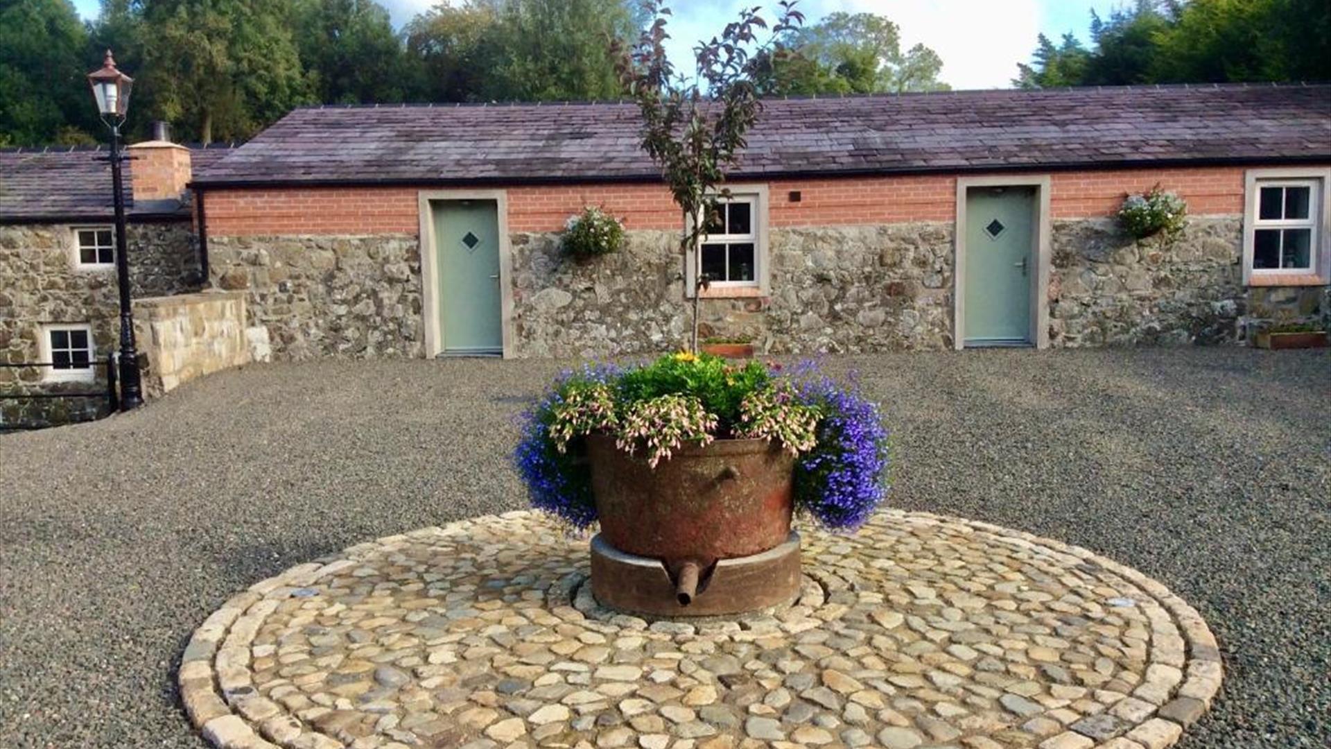 Image shows front of cottages with flower bed in a stone circle
