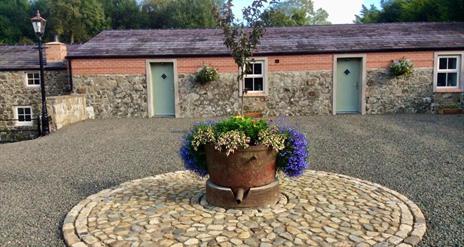 Image shows front of cottages with flower bed in a stone circle