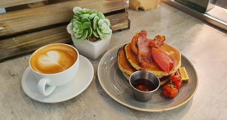 Image shows a cup of coffee and bacon with pancakes at Paul Hampton cafe