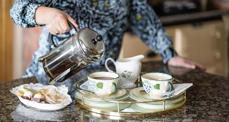 Image with owner pouring tea into cups with buns on a plate