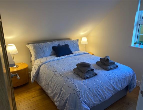 Image shows double bedroom with beside tables and lamps and wooden floor