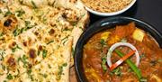 An image of a chicken curry with handmade naan bread and a bowl of rice