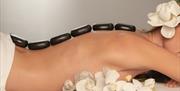 Image is of a lady with stones on her back for a hot stone massage. A display of white orchids are also in the image