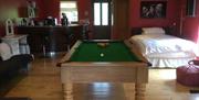 Image shows room with a double bed, sofa, kitchen area and small pool table in the centre of the room