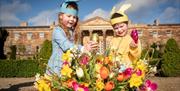Image is of children holding Easter eggs in a basket in front of Hillsborough Castle