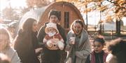 Image shows a family enjoying hot drinks and snacks out doors. Autumnal setting beside glamping pods.